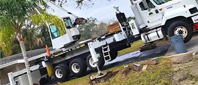 A white boom crane truck set up on a residential street under mature oaks.